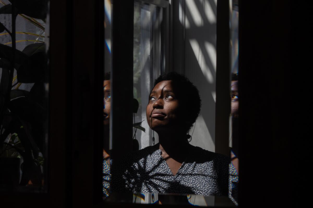 A woman framed in shadows, looking out a window into the sun