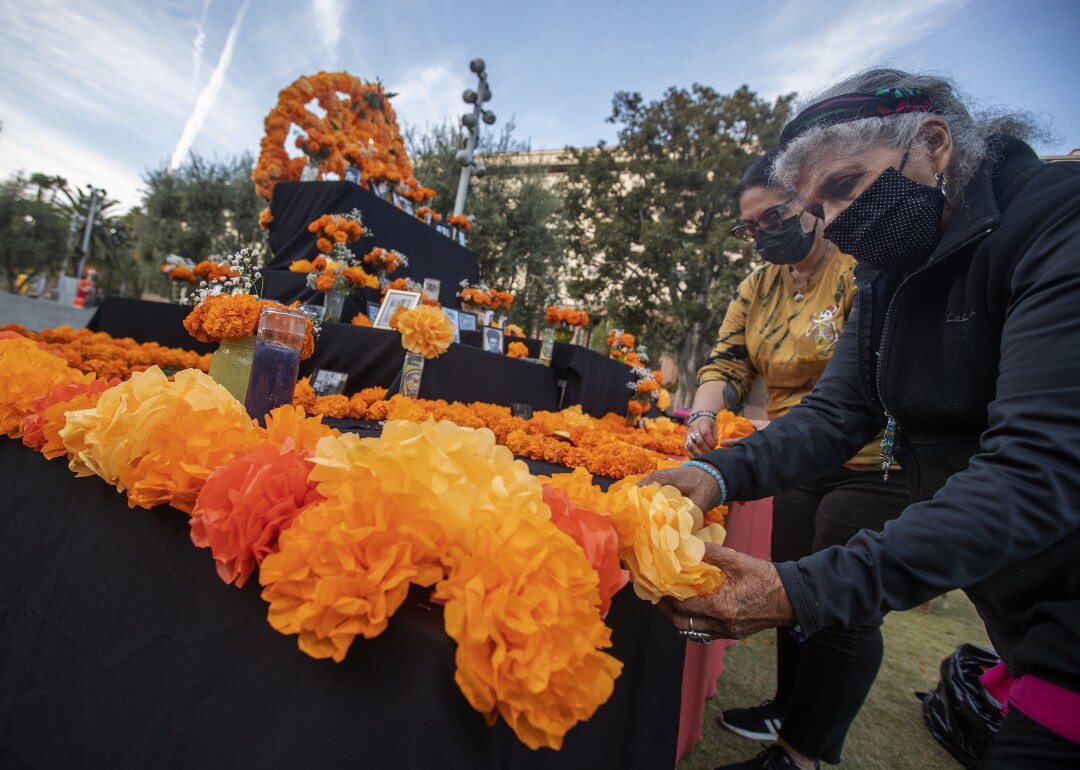 Dos mujeres colocan caléndulas de papel en el altar del Día de Muertos de la comunidad.
