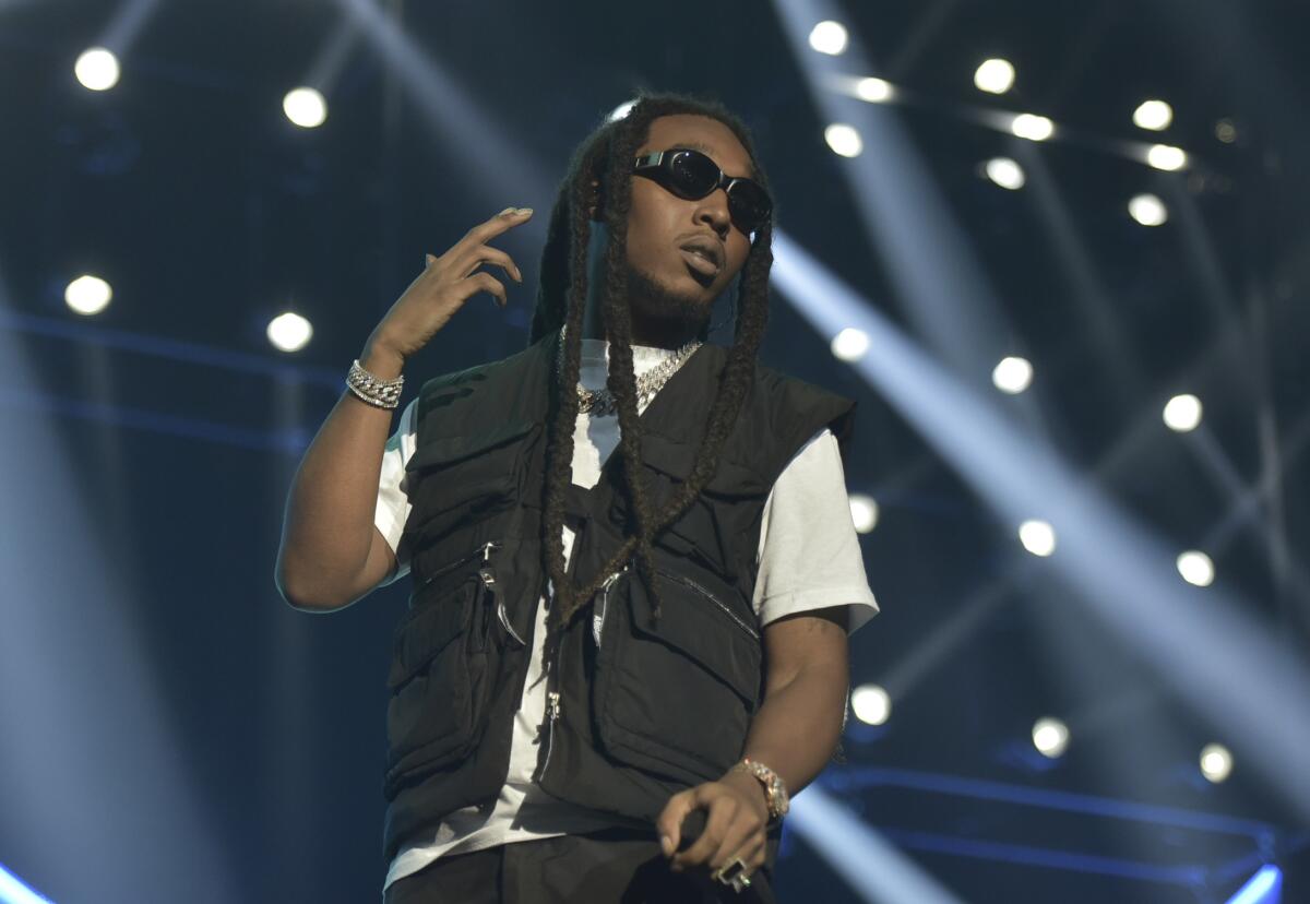 A man with long black hair wearing a black vest and white T-shirt onstage.