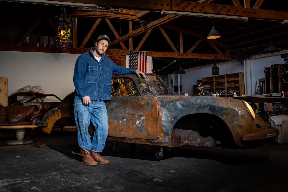 Um homem está ao lado de uma obra de arte feita a partir de um Porsche queimado.