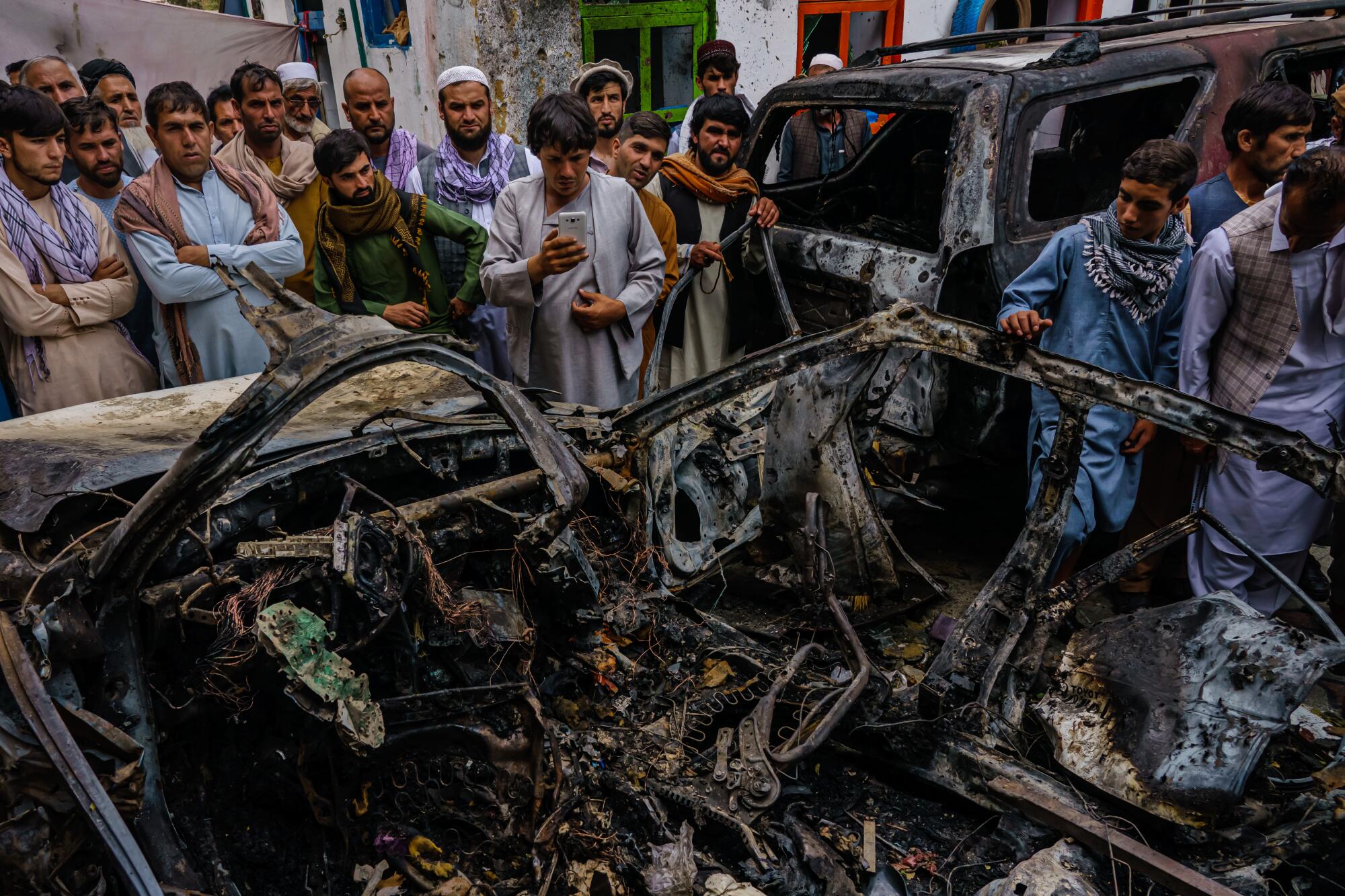 People gathering around burned-out vehicle