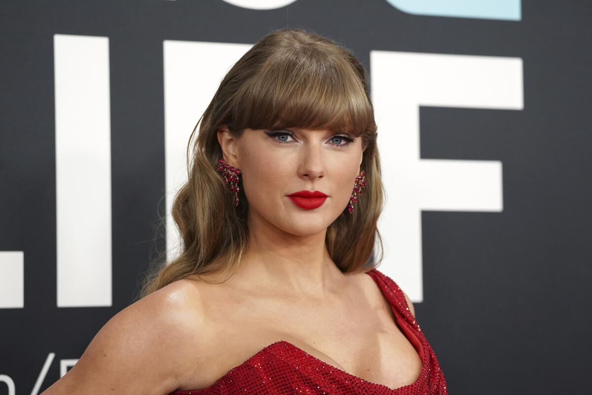 Taylor Swift poses in bright red lipstick and a red dress that has only one shoulder covered