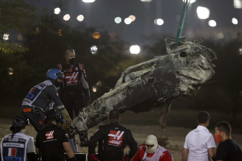 A part of Romain Grosjean's burnt car is removed after the crash while Haas staff watch.