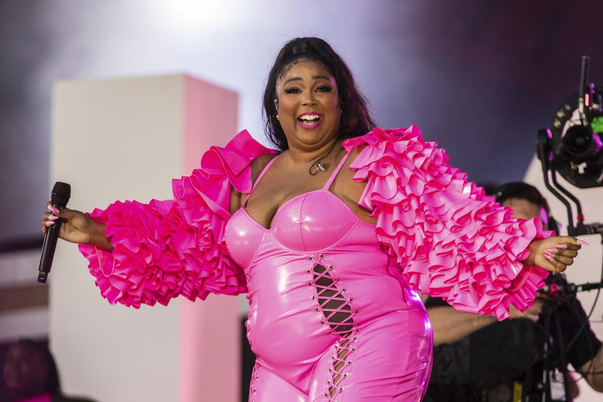 A woman holding a microphone and wearing a hot pink outfit on a stage.