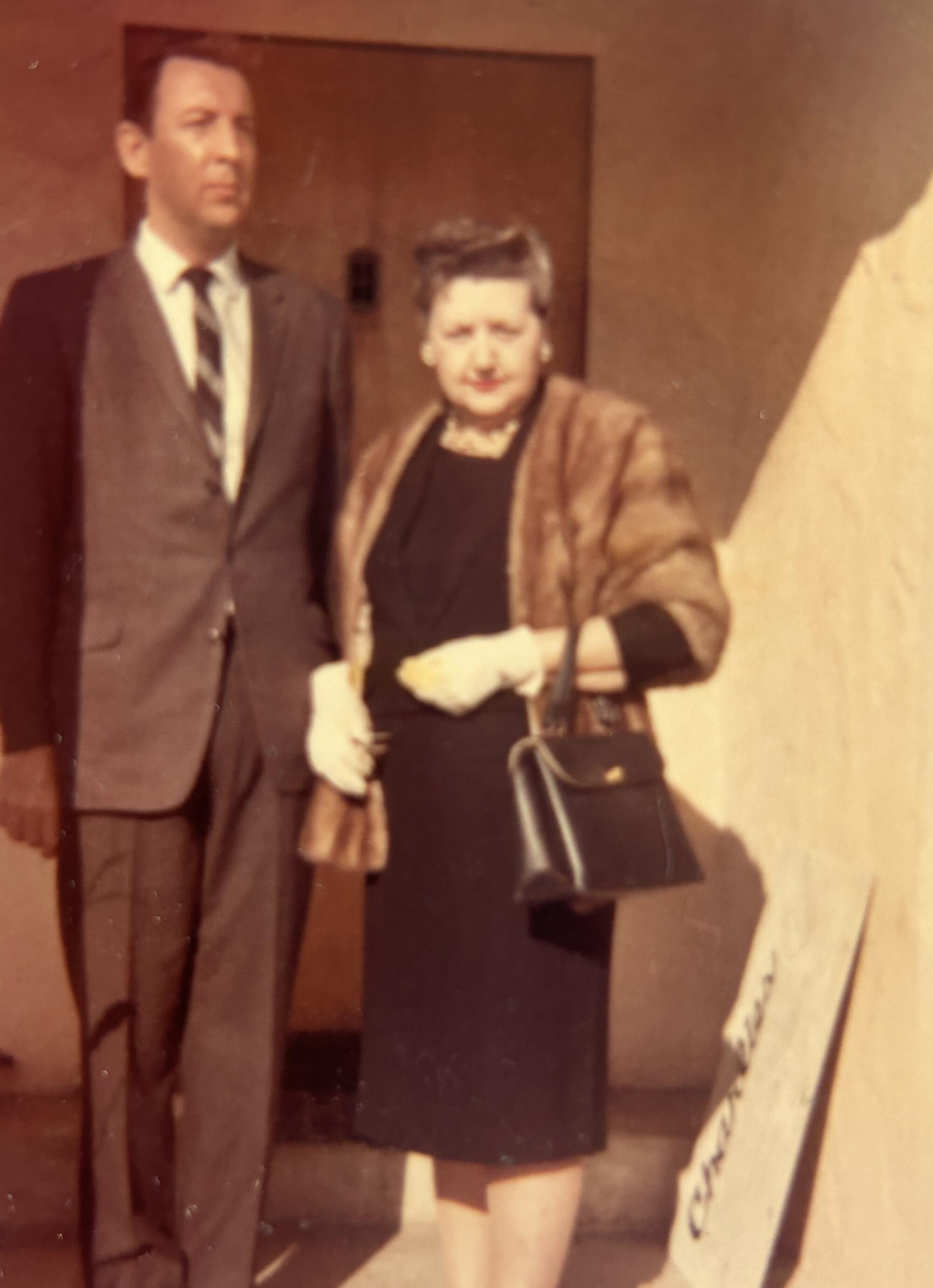 A tall man in a suit and a woman in a fur stole in a sepia-toned photo from the 1950s