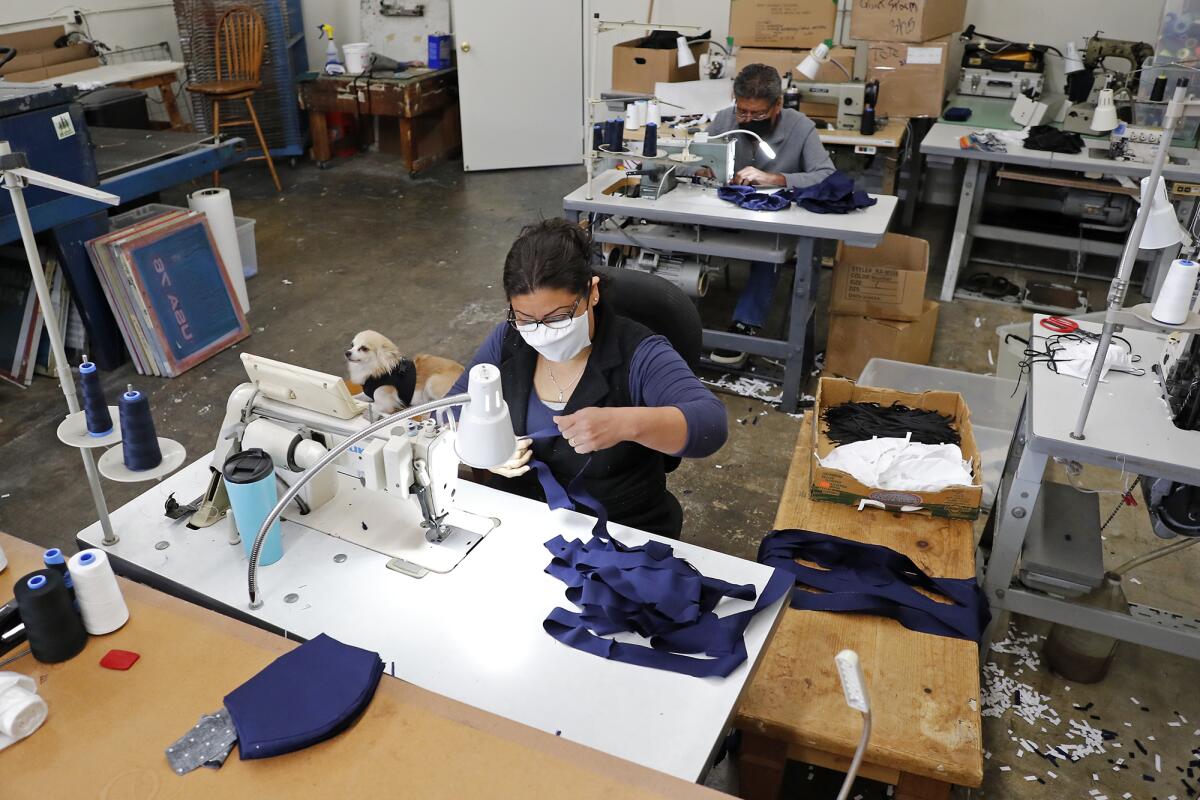 Adali Rogel, foreground, and Santos Sanchez, top, sew face masks in a warehouse in Costa Mesa on Thursday. Grant Broggi, The Strength Co. owner, is selling the masks online and donating them to Stater Bros. grocery stores.