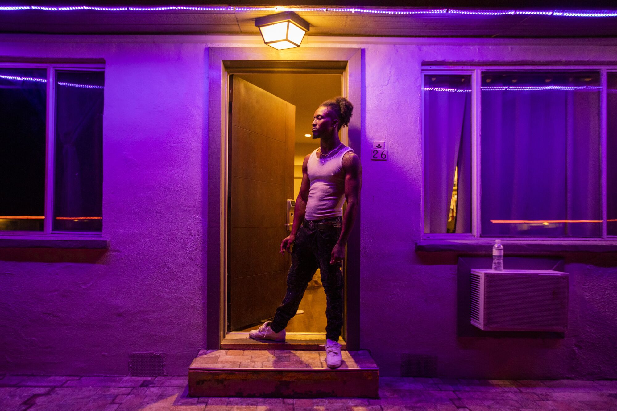 A man stands in a motel room doorway under purple lighting.