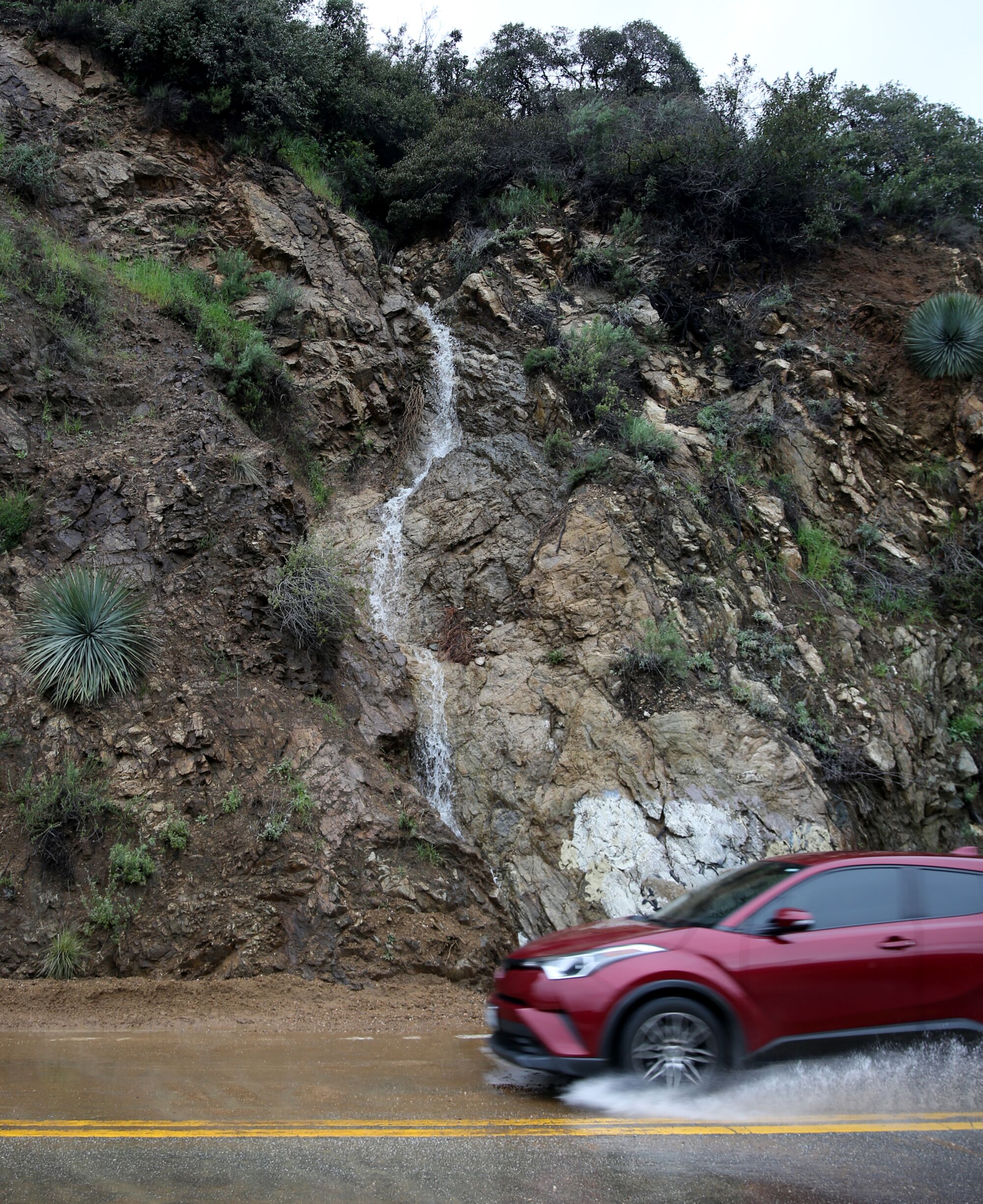 Rare waterfalls appear around Los Angeles after Hurricane 3 A waterfall flows along the road as a car splashes a puddle.