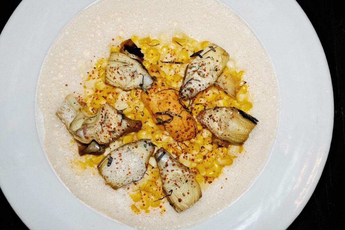Halved baby grilled artichokes with creamed corn and uni in a wide-brimmed white bowl at Darling in West Hollywood.