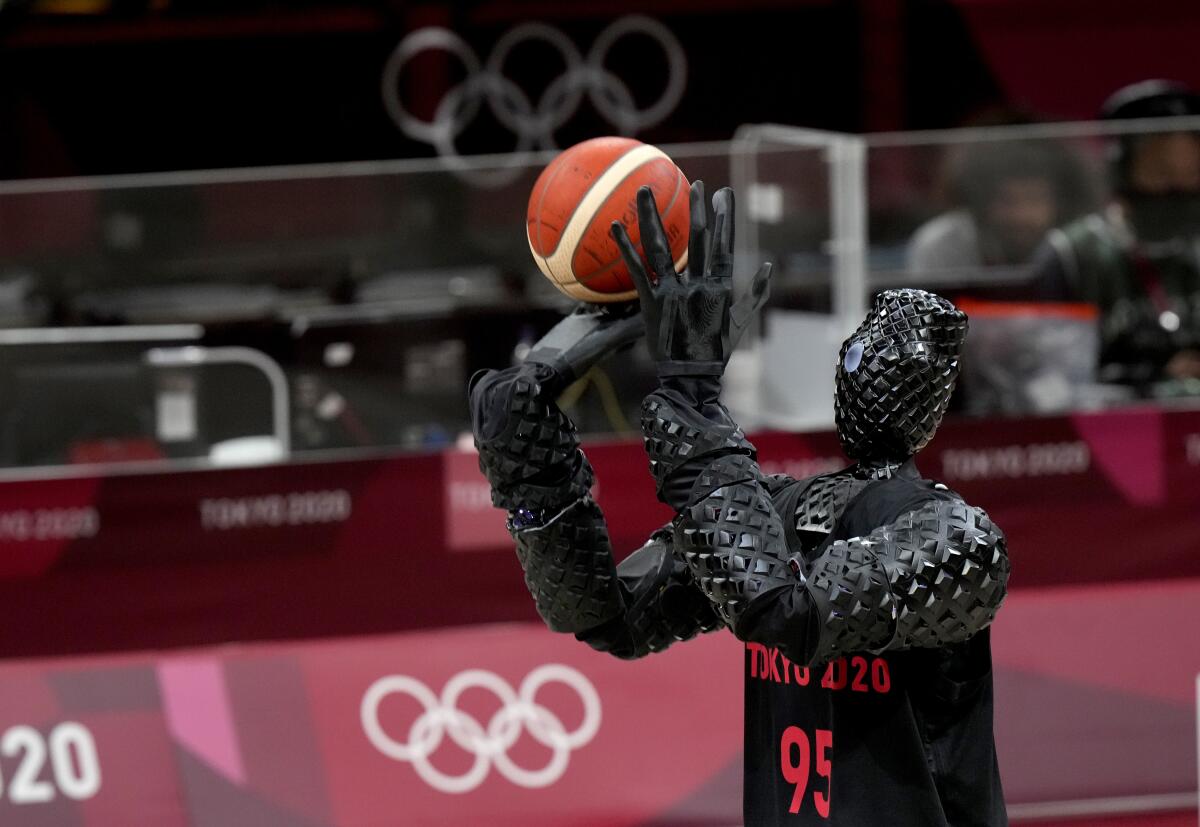 A robot in a basketball jersey stands poised to shoot a basketball.