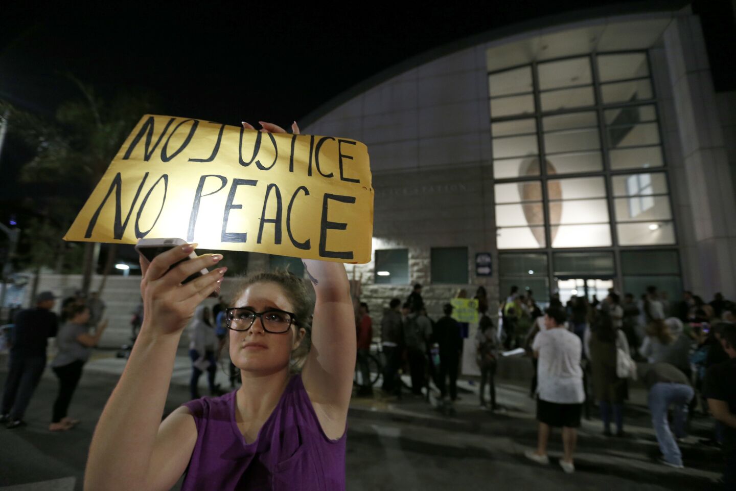 A protester holds a sign in front of the LAPD Newton Divison station on Monday night. Protesters started their march at the site where police fatally shot a Latino man Sunday in South Los Angeles.