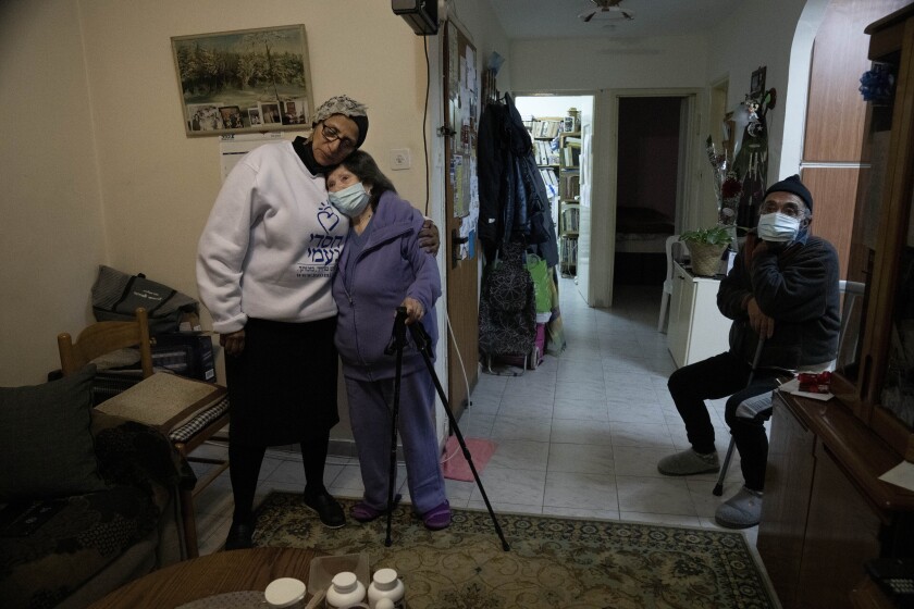 Tshuva Kabra, left, director of the national welfare system at the Chasdei Naomi charity, embraces Holocaust survivor Freida Rovenchim, in her family apartment in Jerusalem, Wednesday, Jan. 26, 2022. Several dozen impoverished elderly Israelis, among them Holocaust survivors, received food donations from the Chasdei Naomi charity, ahead of International Holocaust Remembrance Day on Thursday. (AP Photo/Maya Alleruzzo)