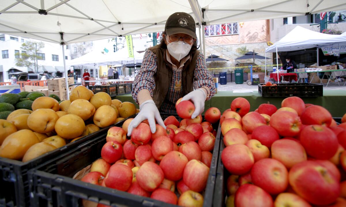 In this file photo, Kyung Jun with Jacy Farm stocked fresh fruits for her customers at the Farmers Market in Little Italy. Employees at grocery stores are required to wear a cloth mask covering their face, and a new order will require food servers, child-care providers and people who work in banks and public transportation to also cover the faces beginning Monday.