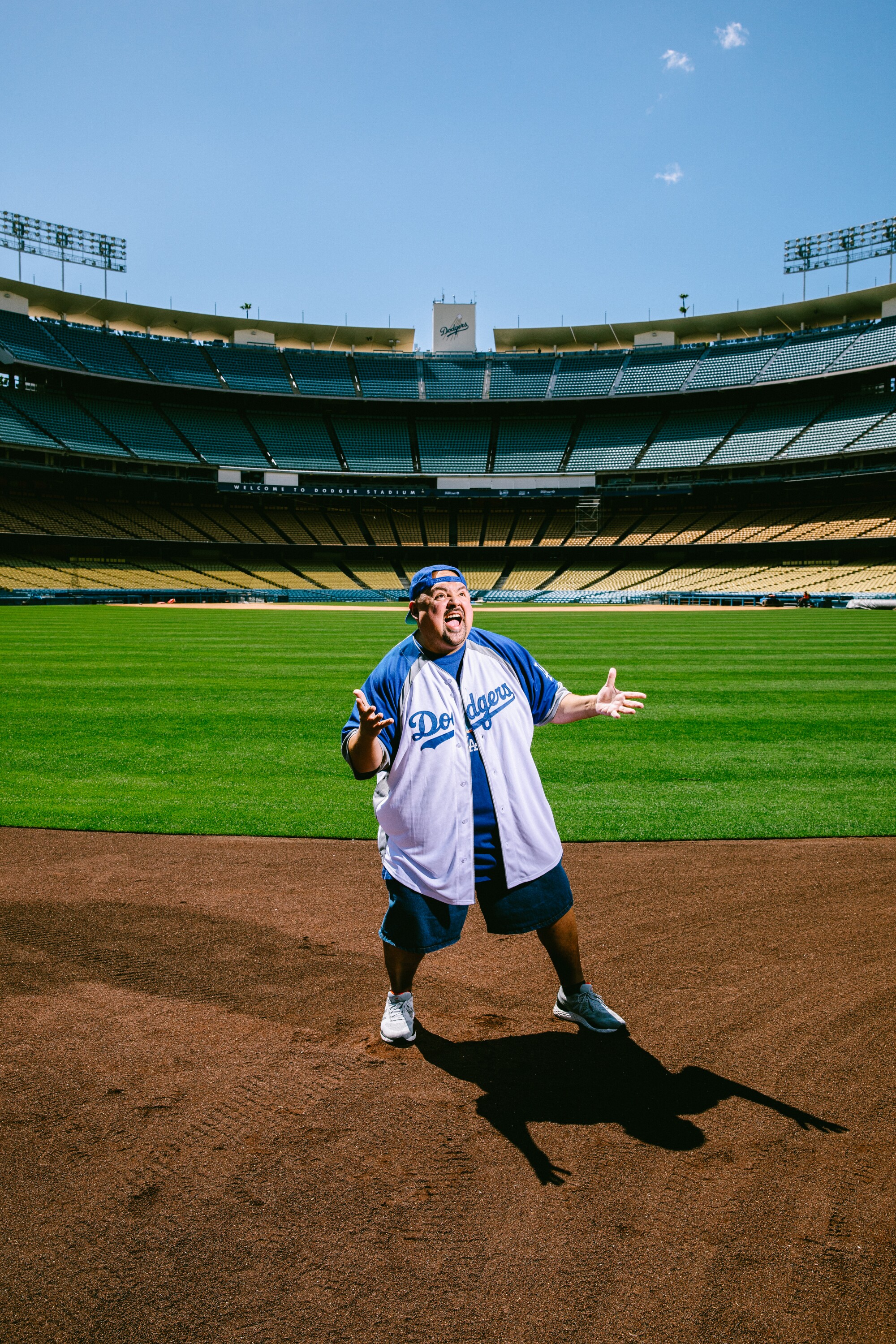 A man poses in Dodgers gear on a sunny day on the field at Dodger Stadium