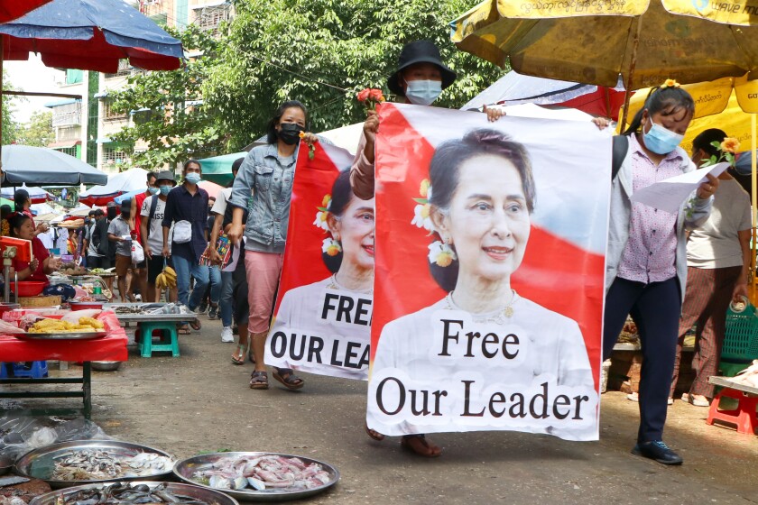 FILE - Protesters walk through a market with posters of ousted Myanmar leader Aung San Suu Kyi at Kamayut township in Yangon, Myanmar Thursday, April 8, 2021. Suu Kyi went on trial Monday, May 2, 2022, in a new corruption case against her, alleging she took $550,000 in bribes from a construction magnate. Suu Kyi has been detained since the army ousted her elected government in February 2021 and has not been seen or allowed to speak in public since then. (AP Photo)