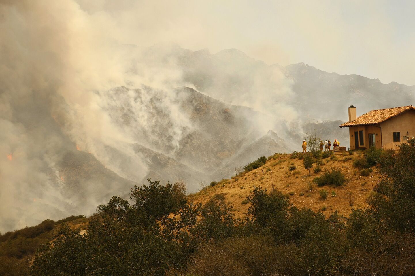 Firefighters watch smoke rise from the Springs fire in the mountains above Malibu.