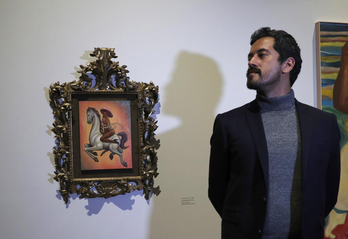 El artista mexicano Fabián Chaírez se para al lado de su pintura que muestra al héroe de la Revolución Mexicana Emiliano Zapata desnudo a horcajadas sobre un caballo, con tacones altos y un sombrero rosa de ala ancha, durante una entrevista en el Palacio de Bellas Artes de la Ciudad de México, el miércoles, 11 de diciembre de 2019.
