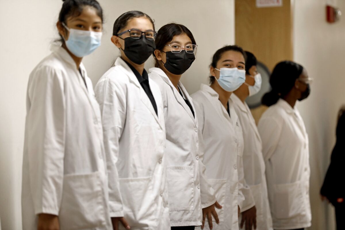 L.A. students in white lab coats wait to greet a visiting dignitary.