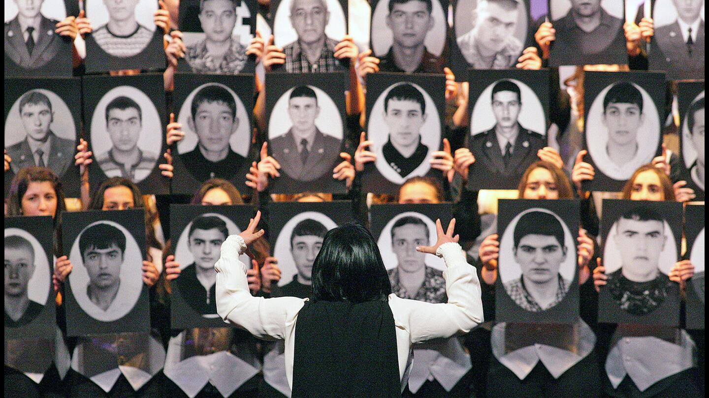 The director of the Rose and Alex Pilibos Student Choir directs a section of the choir who are holding portraits in front of them at the city of Glendale's 15th annual Armenian Genocide commemoration at the Alex Theatre in Glendale on Friday, April 22, 2016.