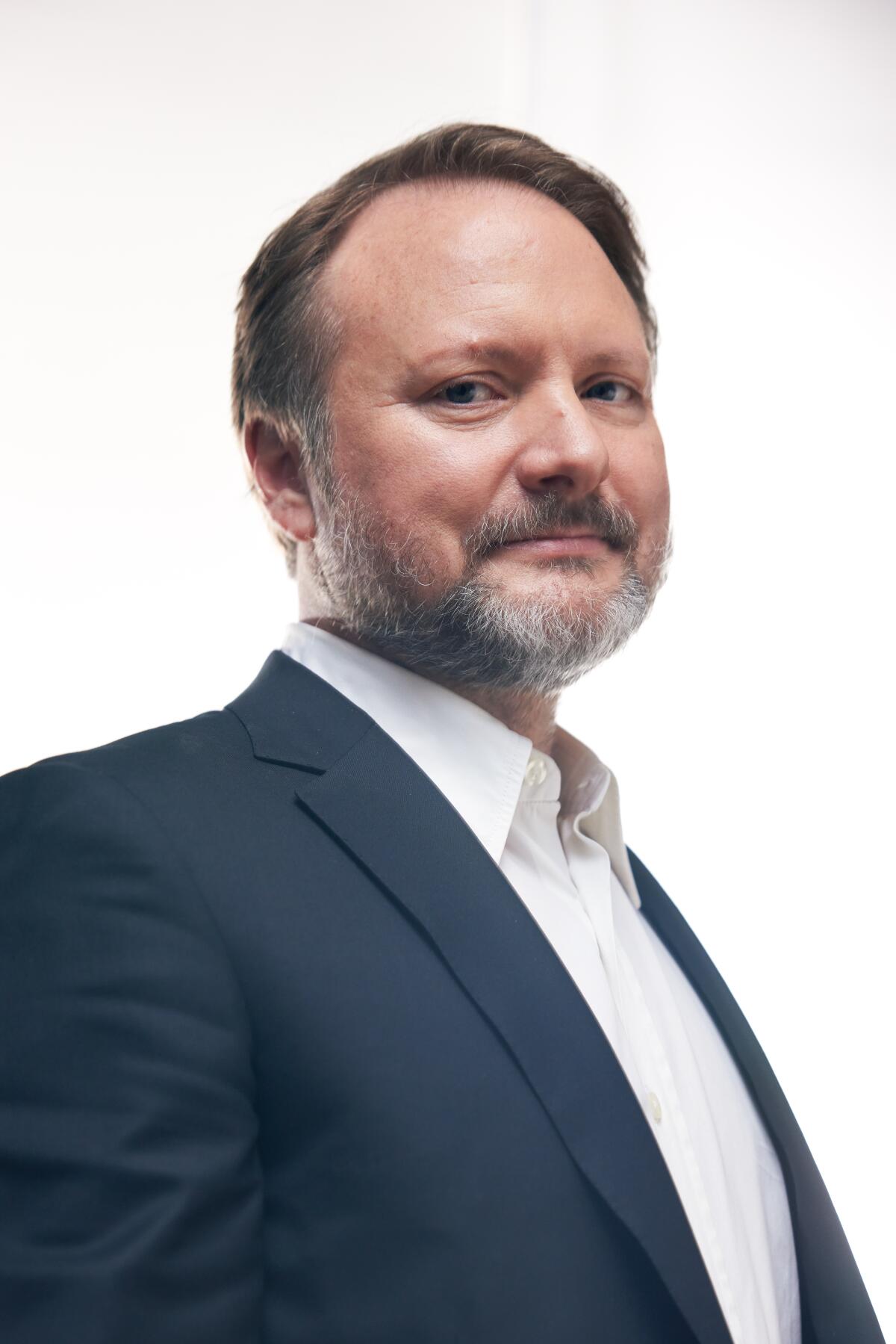 Rian Johnson in a dark suit jacket looks into the camera for a portrait.