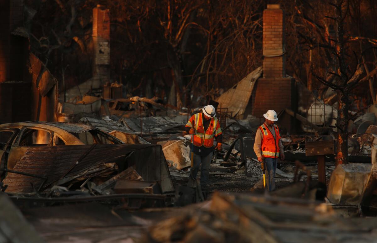 Pacific Gas & Electric Co. workers make their way through the fire-ravaged neighborhood of Coffey Park in Santa Rosa on Saturday.