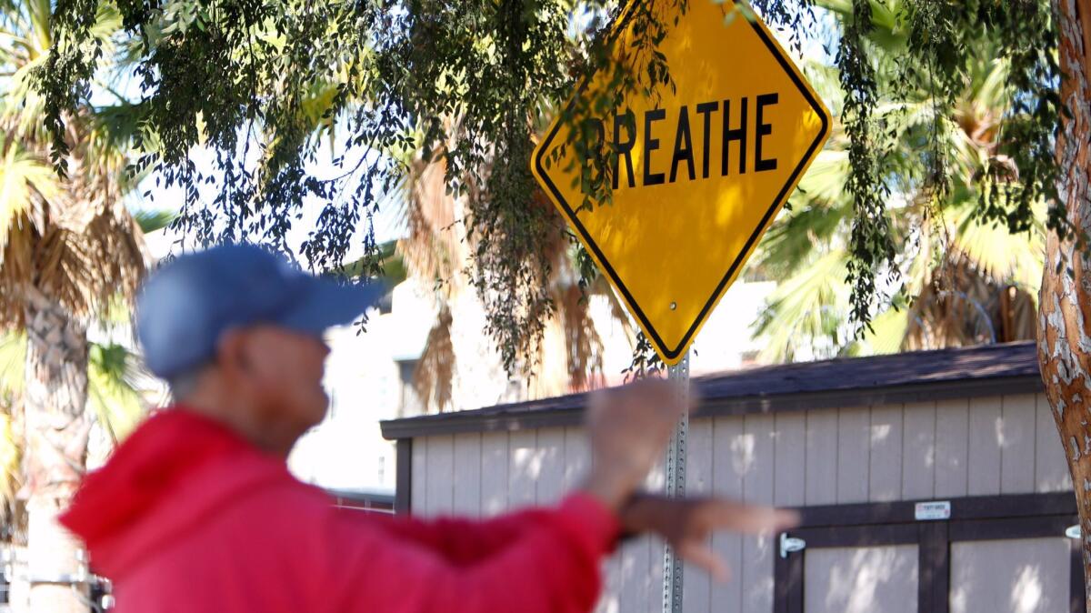 A man does Tai Chi near a street sign multimedia art piece with the word "Breathe" in Central Park.
