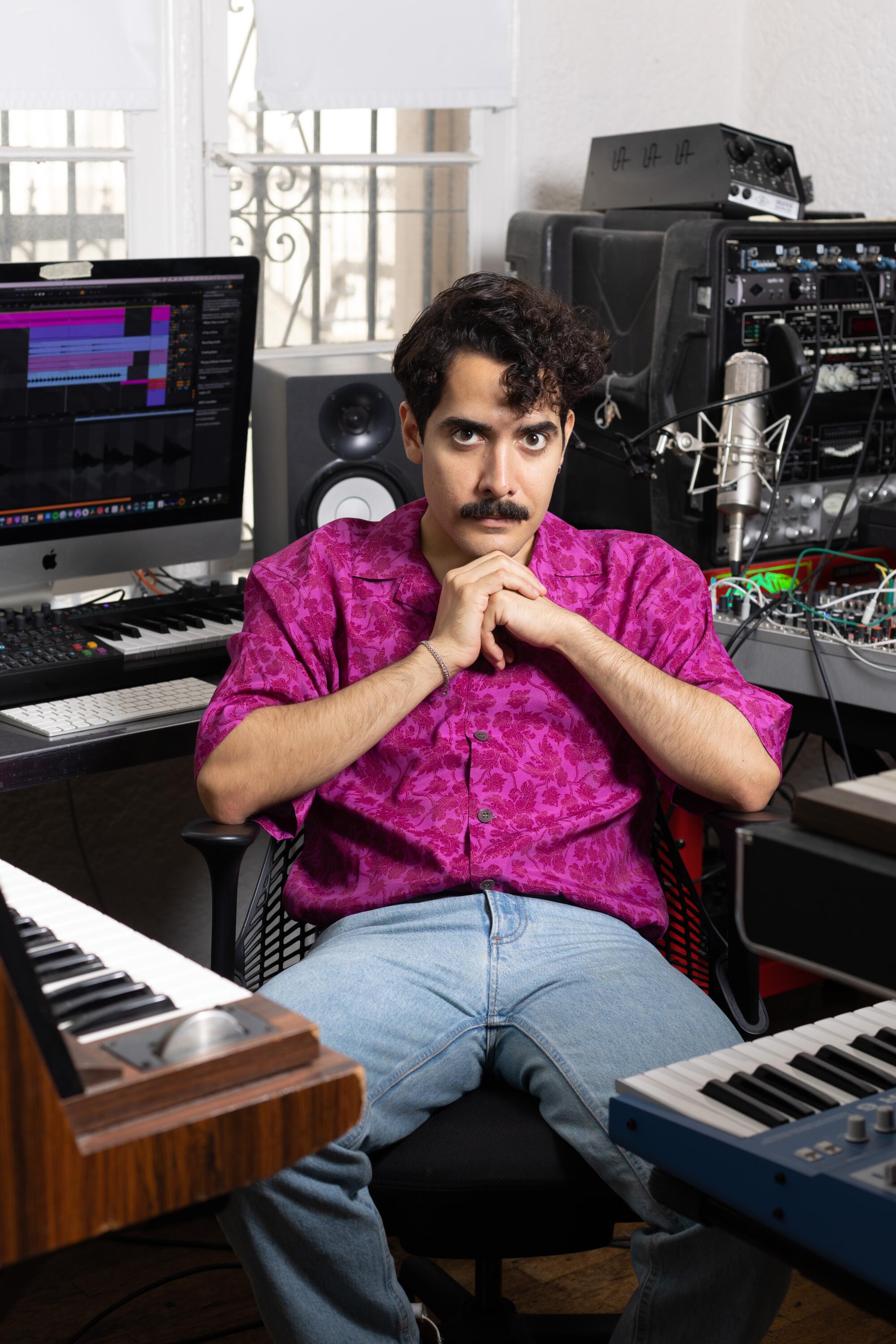 Alan Palomo rests his chin on his hands as he sits among his keyboards.