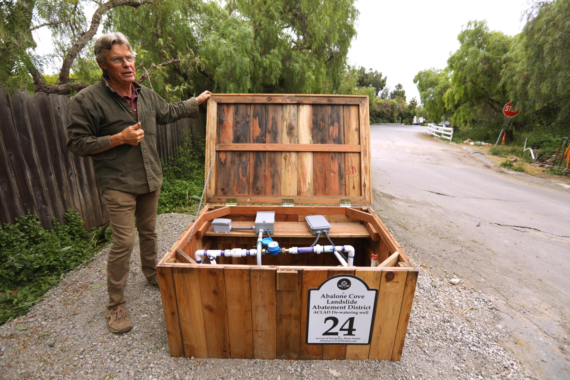 A man stands near a knee-high wooden enclosure housing pump equipment.