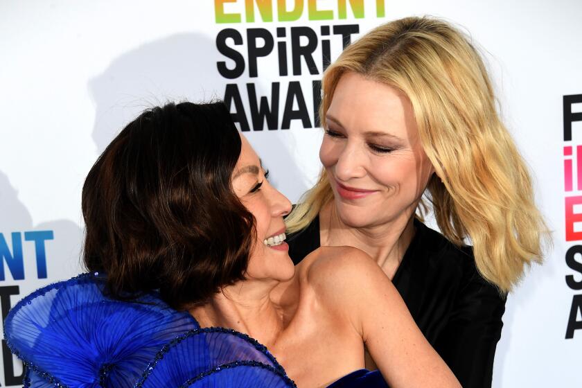 Two women smile at one another and embrace upon arrival at a red-carpet event