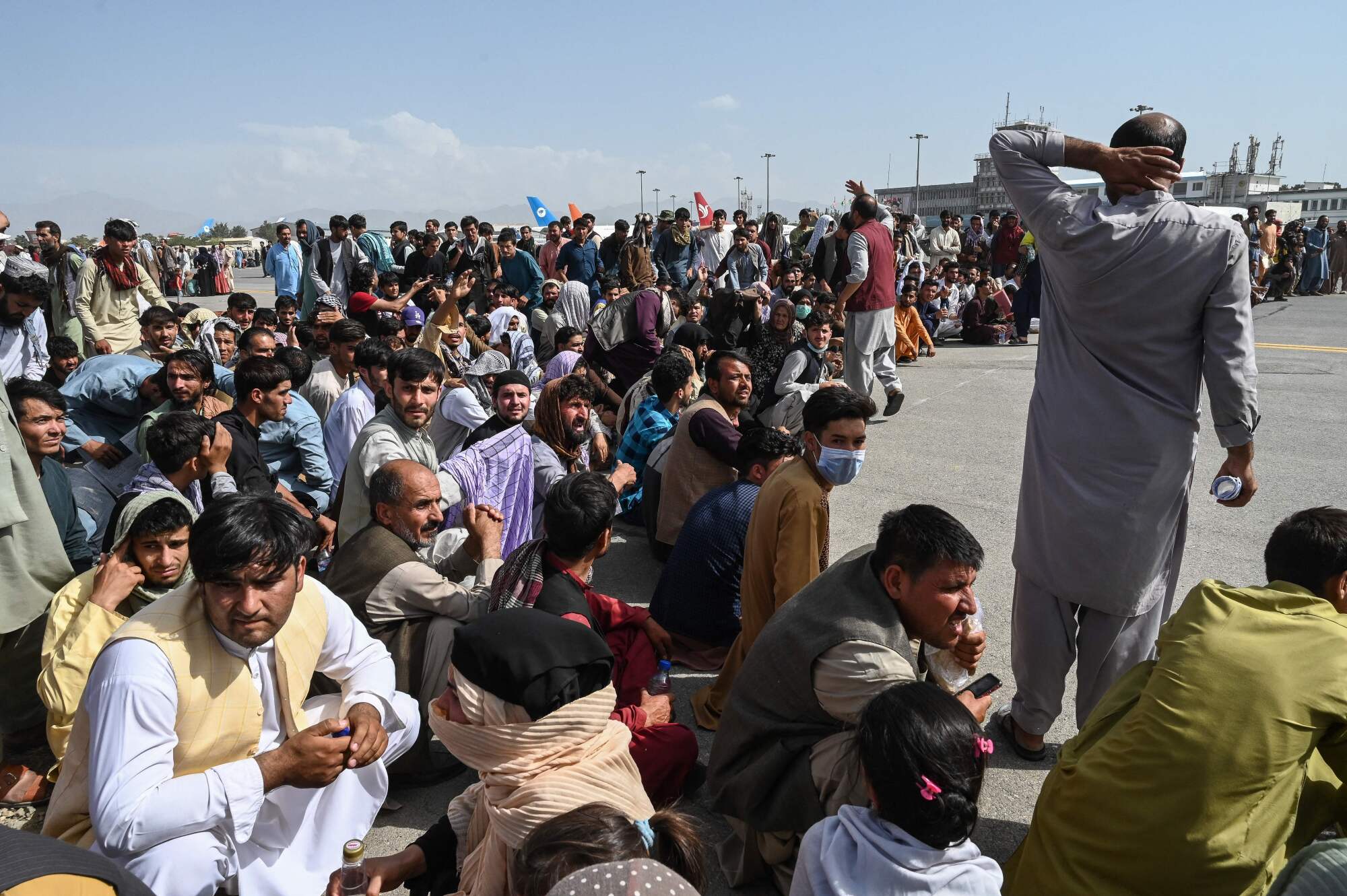 A large group of Afghans sits on paved ground 