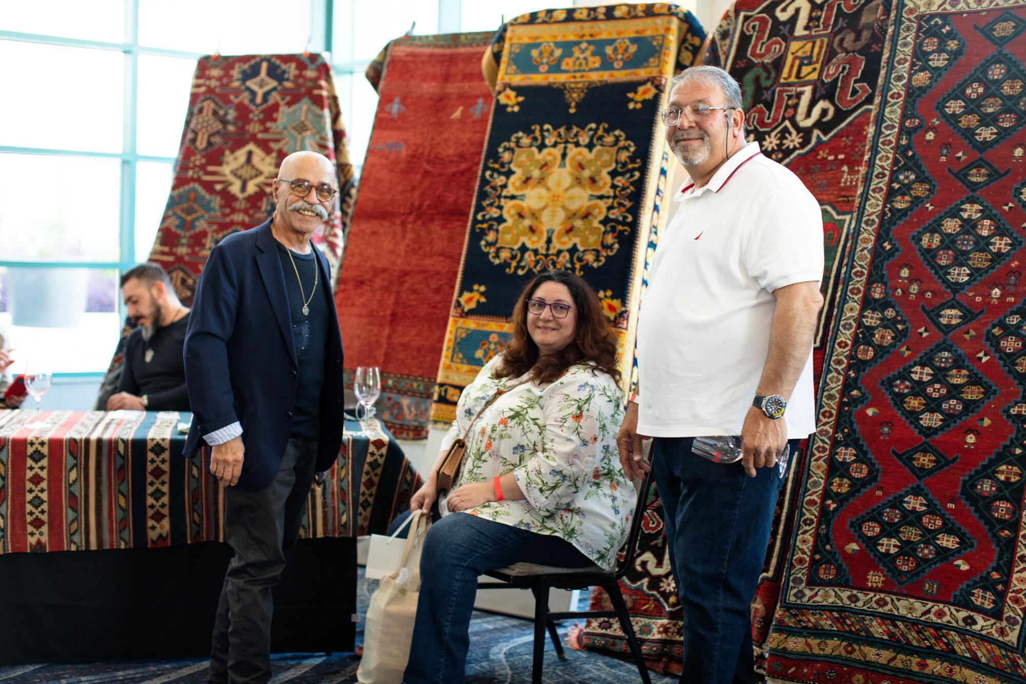 Two men and a woman in front of a display of handcrafted rugs.