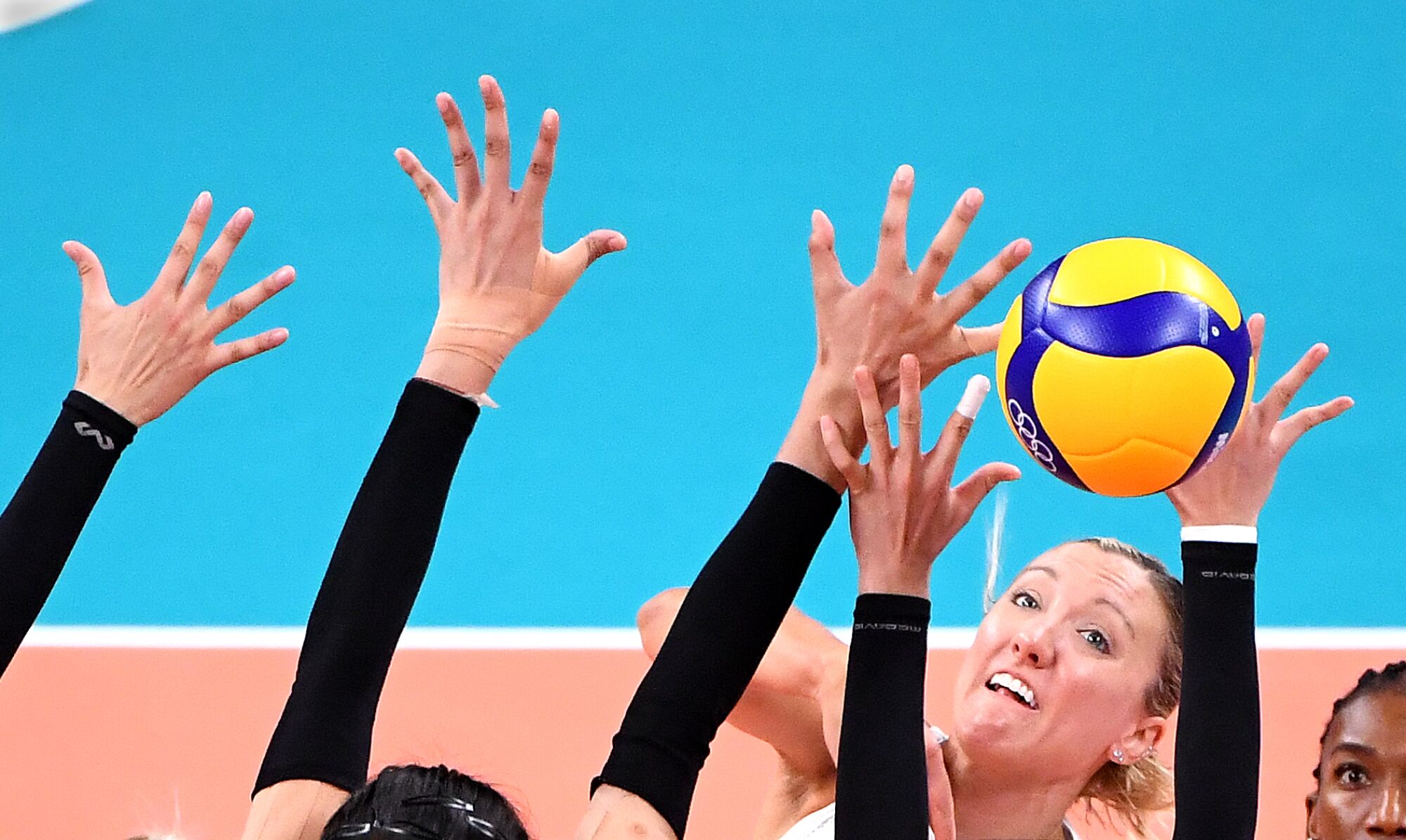 A woman leaps for a volleyball amid numerous outstretched arms.