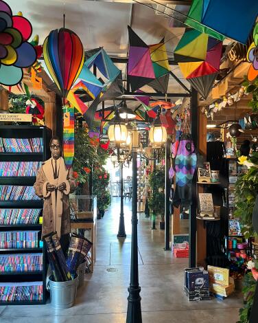 Rainbow-colored kites hang from the ceiling of a bookstore with old-timey street lamps in the aisle