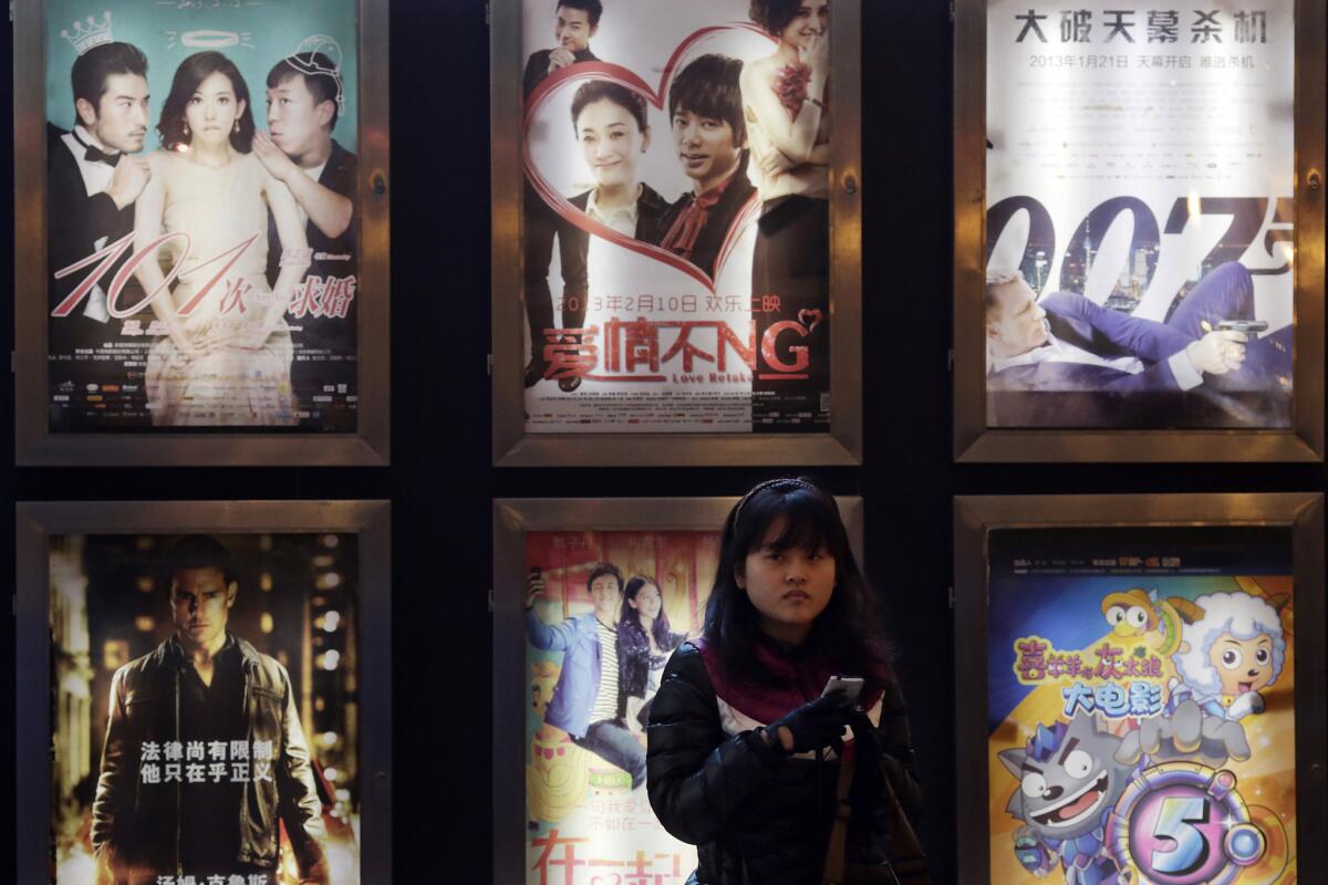 A woman stands in front of the advertisements of Chinese and foreign films on showing at a movie theater in China, where theater owners are being prosecuted for underreporting box office revenues.