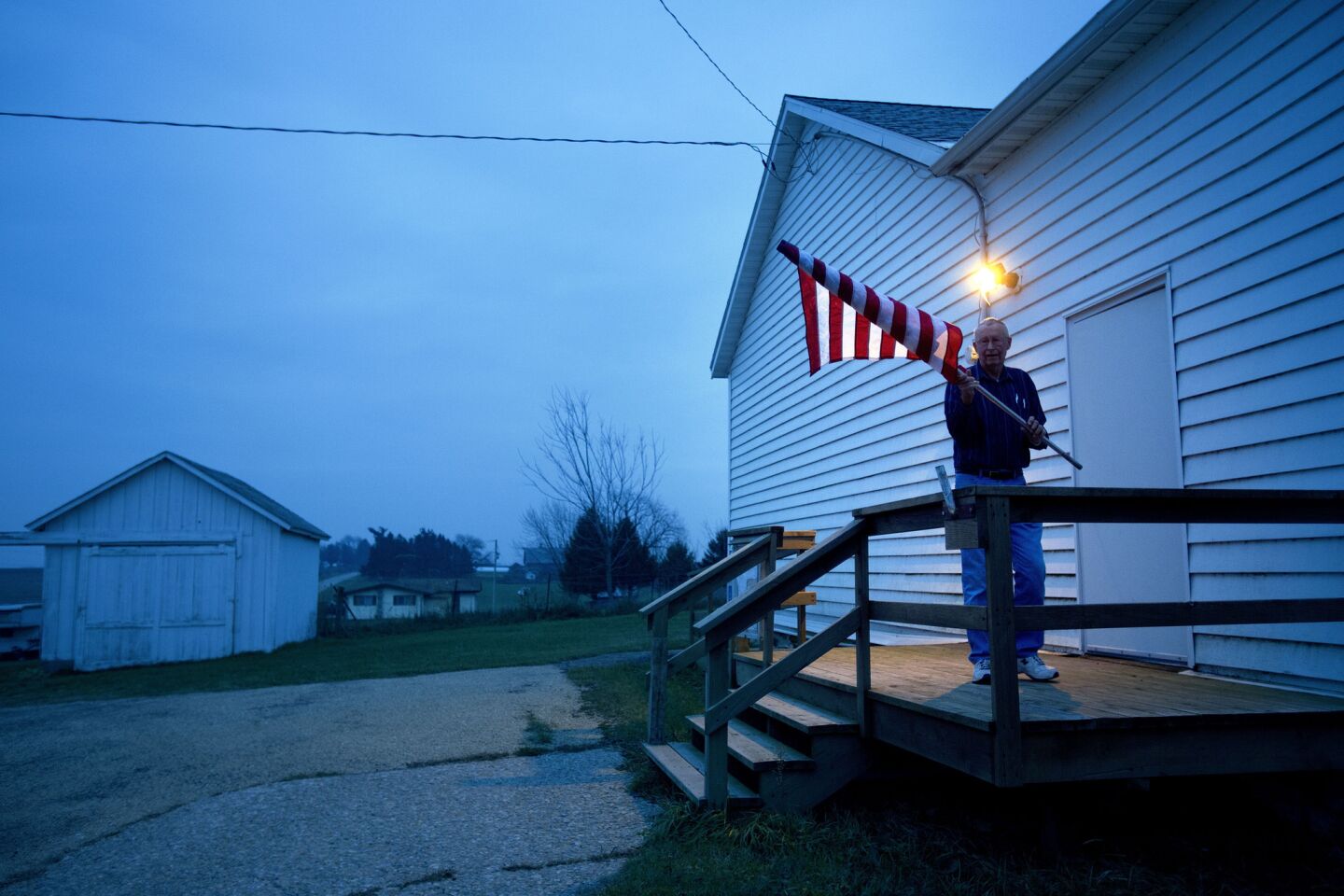Election Inspector Jim Nodorft unfurls the American flag to hang it outside the Smelser Town hall before polls open at 7 a.m. in Georgetown, Wis.