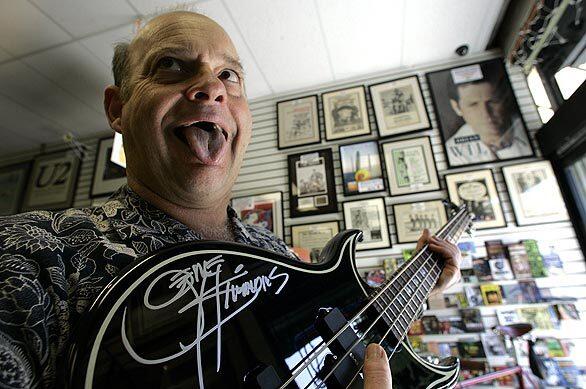 Imitating Gene Simmons, Wayne Johnson of Rockaway Records shows a bass guitar autographed by the member of the rock group KISS.
