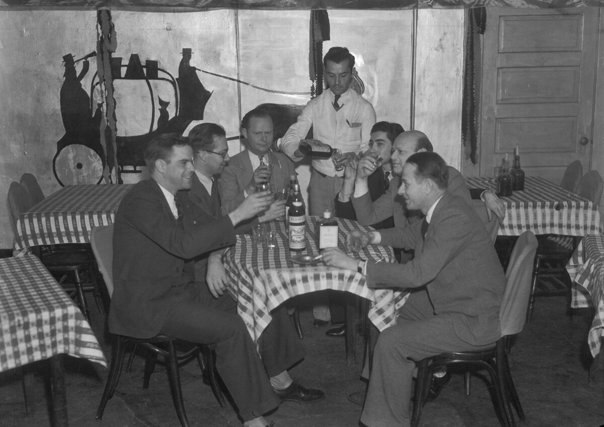 Men sit around a table sharing drinks as a waiter pours. 