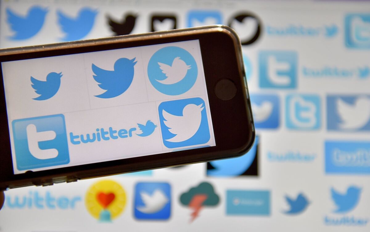 Twitter logos are displayed on a cellphone, against a background of Twitter logos.