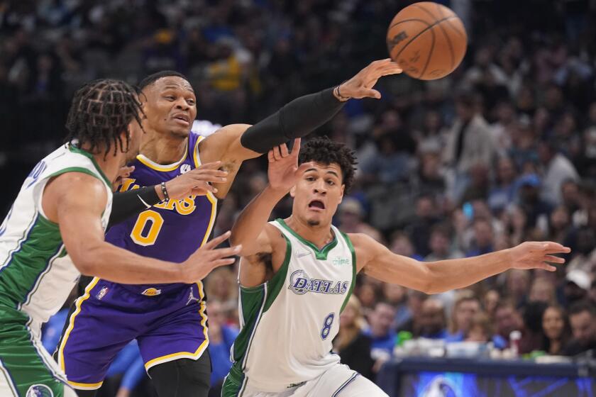 Los Angeles Lakers guard Russell Westbrook (0) passes off between Dallas Mavericks defenders Josh Green (8) and Jalen Brunson during the first half of an NBA basketball game in Dallas, Tuesday, March 29, 2022. (AP Photo/LM Otero)