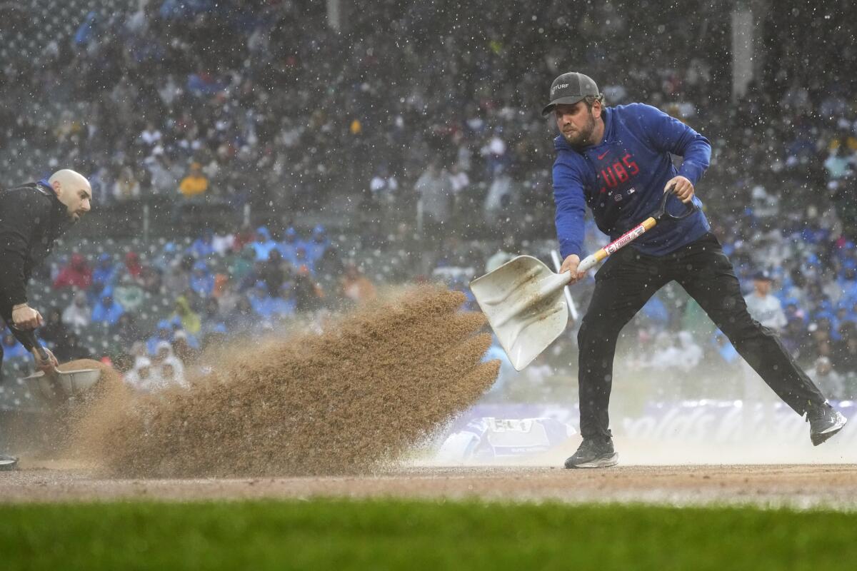 A Cubs grounds crew worker shovels sand during a rain delay at Wrigley Field on Sunday.