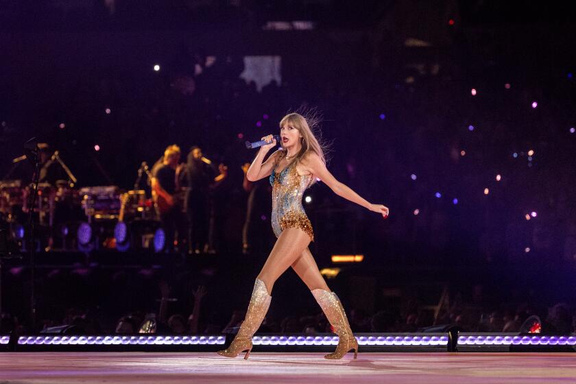 Taylor Swift in a bedazzled leotard and matching boots strutting on a stage while holding a microphone