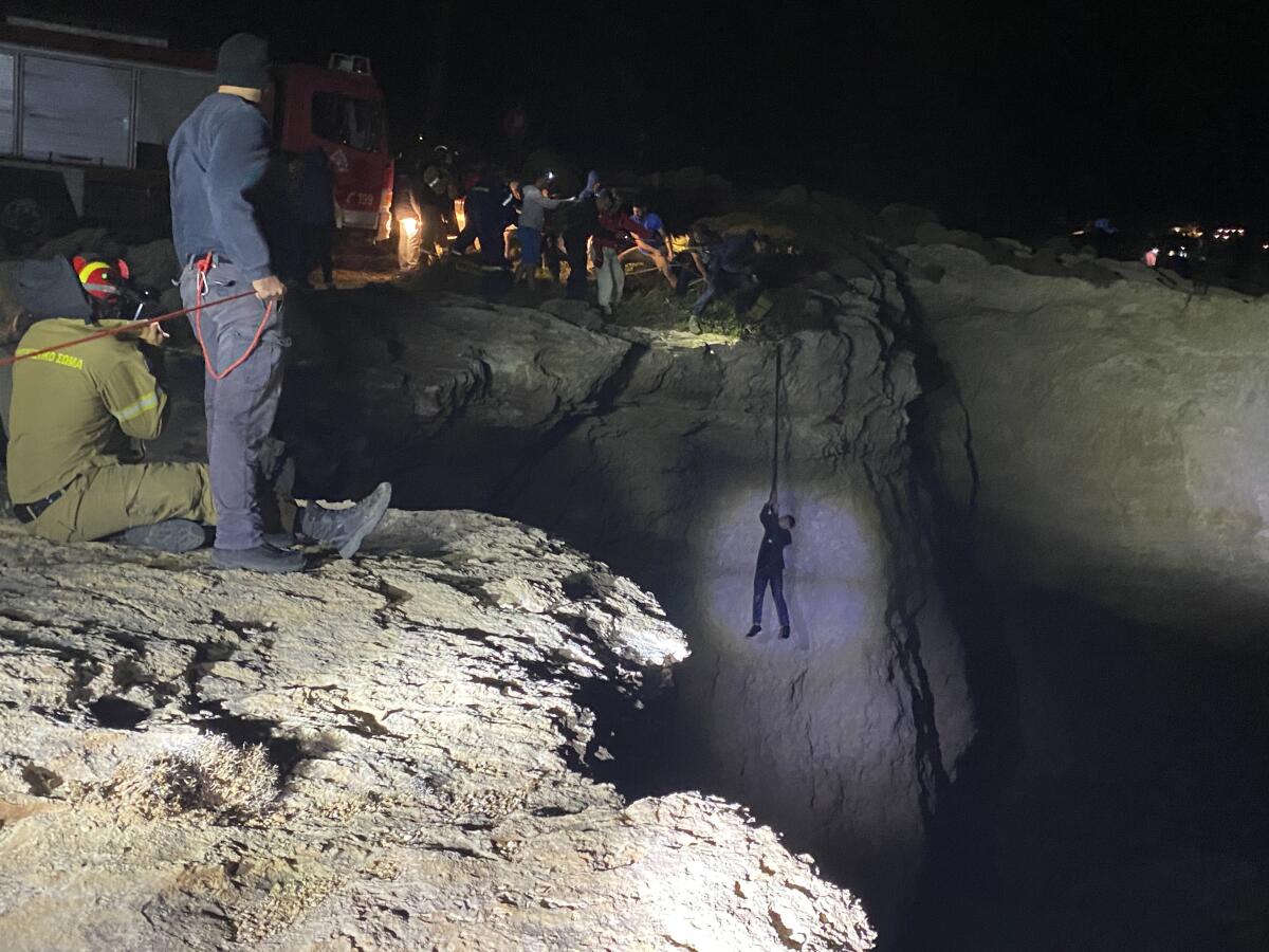 A person holds on to a line as rescuers pull them up a cliff, illuminated by spotlights.