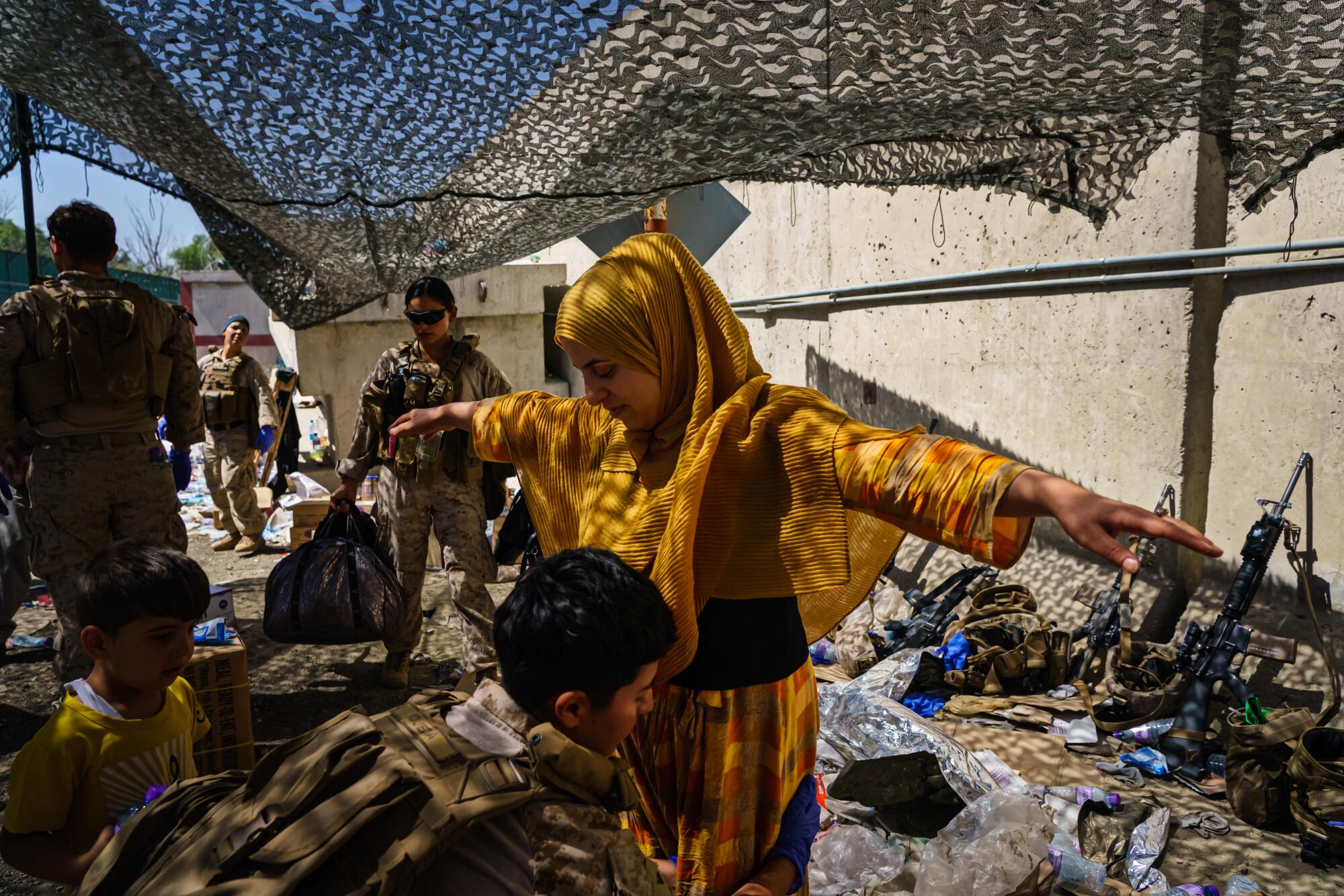 A soldier pats down a woman wearing a golden yellow burqa