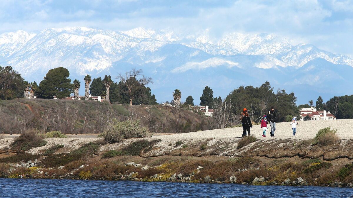 Visitors to the Bolsa Chica Wetlands enjoy a chilly, blustery day beneath puffy clouds and a backdrop of the snow-covered San Gabriel Mountains.