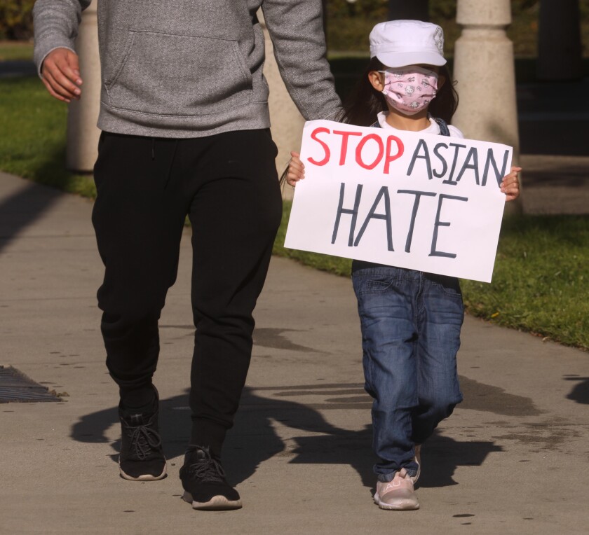 A child in a mask carries a sign that says 'Stop Asian Hate.'