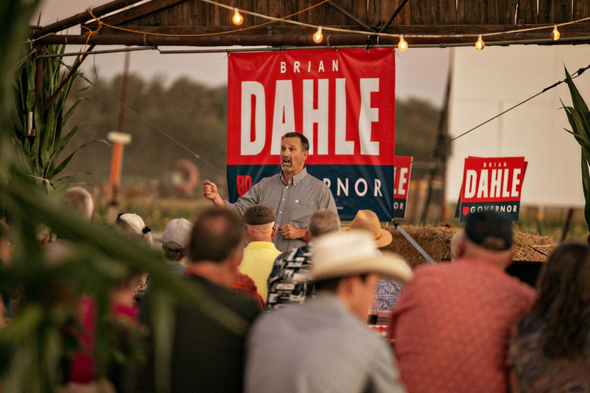 A man stands below a banner and talks to a crowd of people.