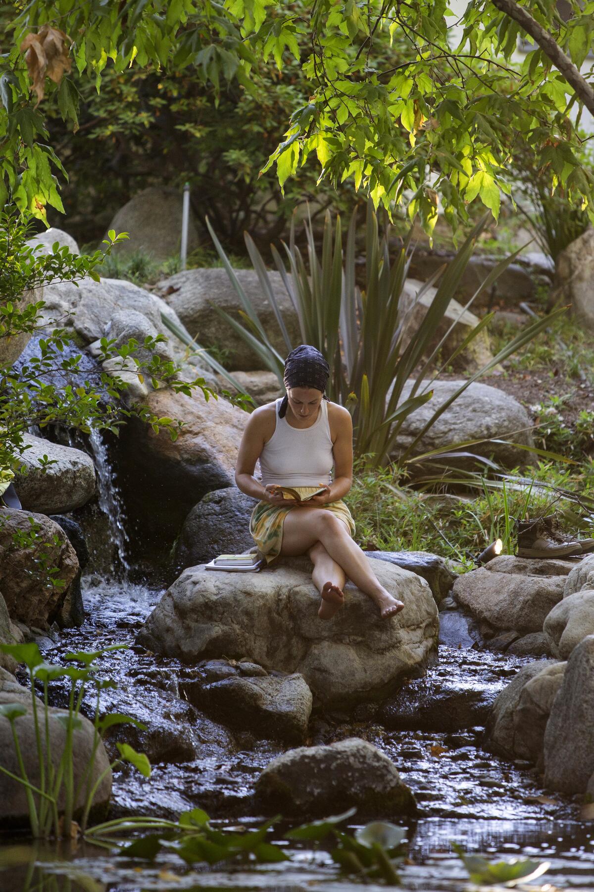 A woman reads next to a small waterfall