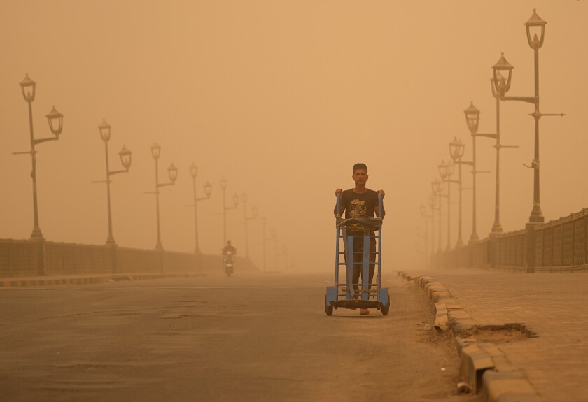 Un hombre empuja una carretilla durante una tormenta de arena el lunes 23 de mayo de 2022, en Bagdad, Irak.