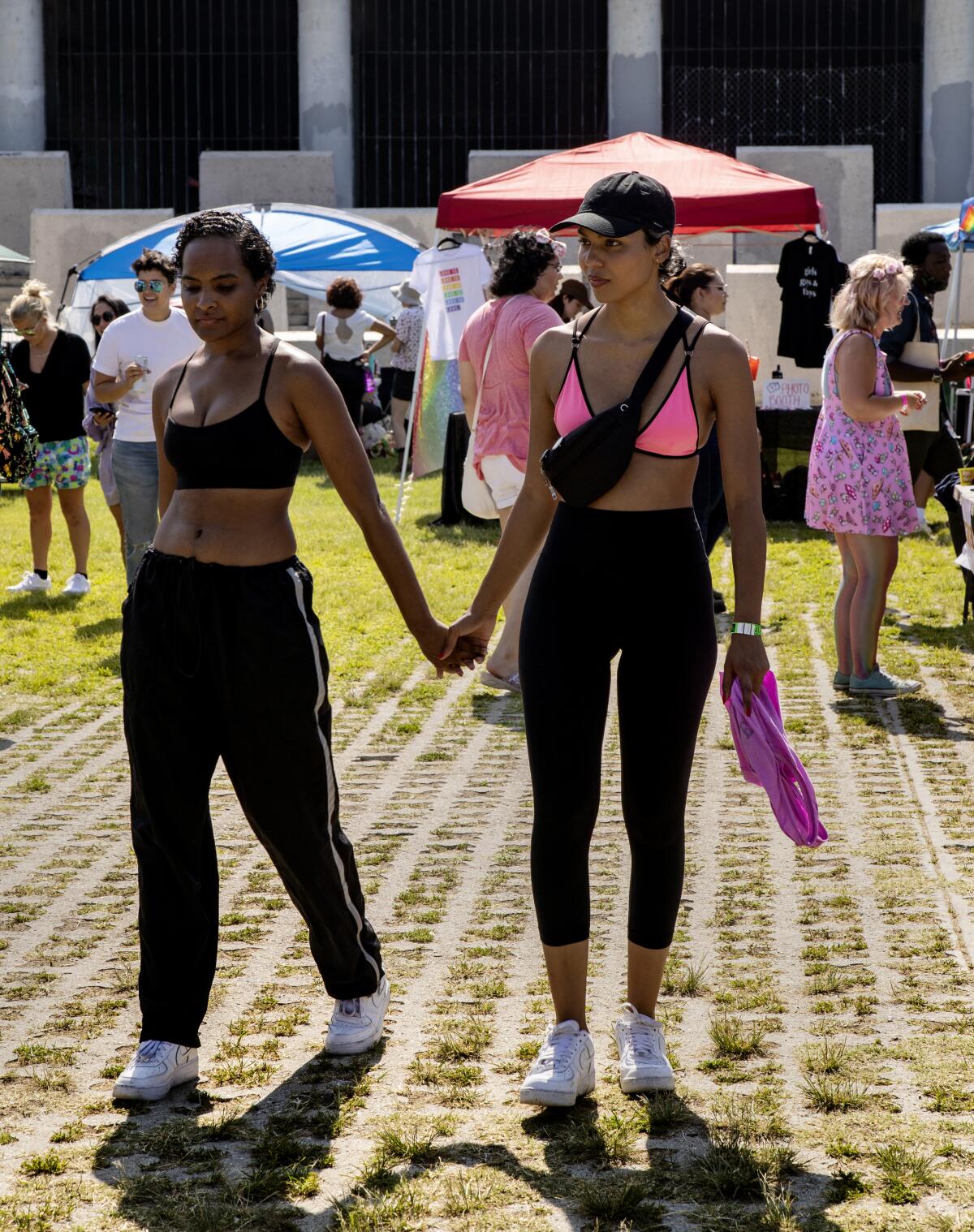 A couple, both in black pants and a sports bra, holds hands