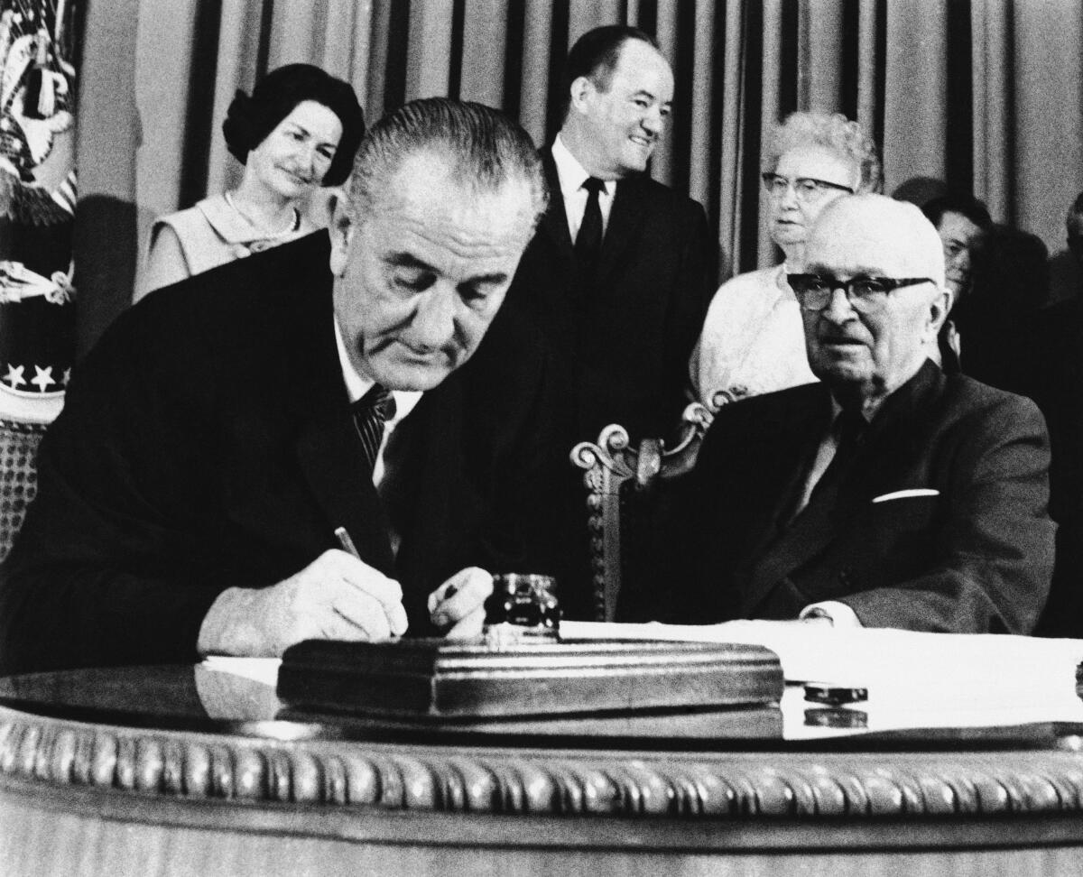 President Lyndon Johnson signs the Medicare bill into law while former President Harry S. Truman, right, observes.